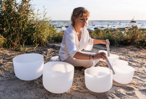 mid aged woman is playing singing crystal bowls at the sea shore