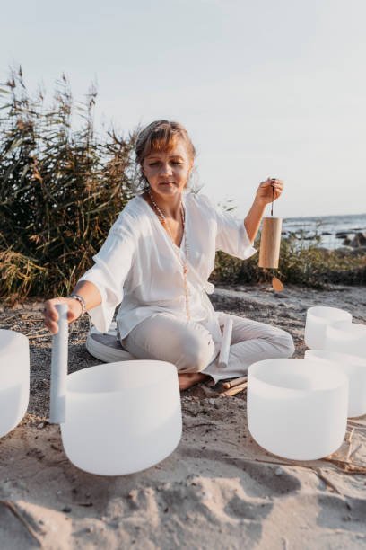 smiling yoga teacher playing singing crystal bowls at the beach in summer